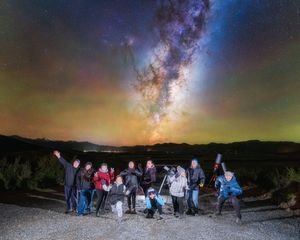 Group of people stargazing with telescopes under the Milky Way galaxy in a dark sky location at night.