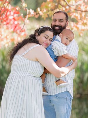 A happy family of three, parents lovingly embracing their baby boy outdoors with colorful autumn foliage.