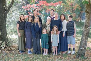 Multi-generational family portrait outdoors in autumn park, smiling group of adults and children among colorful fall foliage.