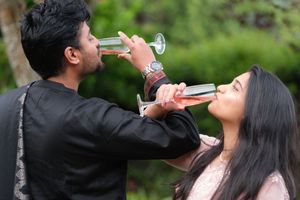 A couple sharing drinks outdoors, man in black outfit and woman in pink enjoying beverages together.
