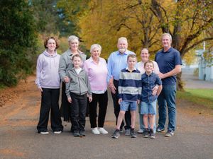 Multi-generational family portrait outdoors in autumn, smiling group of adults and children on a tree-lined path.