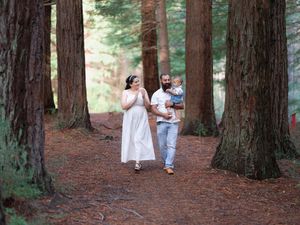 Family walking through redwood forest, mother in white dress, father carrying toddler on woodland path.