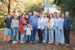 Large multigenerational family group portrait outdoors in autumn park setting with colorful fall foliage background.