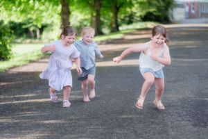 Children playing and walking together on a tree-lined path in summer.