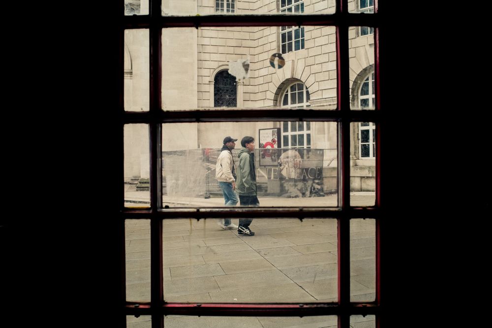 A view through window panes of people walking past a stone building exterior.