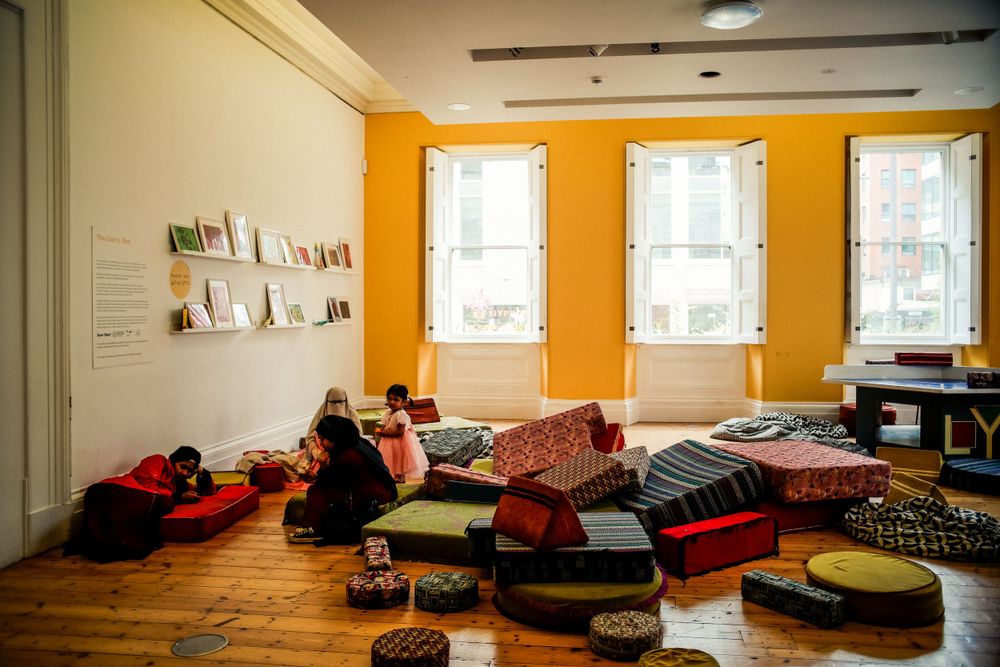 A bright yellow room with white windows, wooden floors and cushions scattered around.