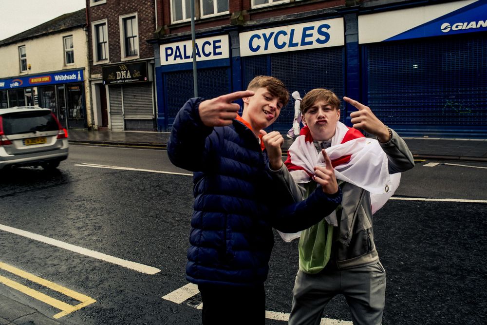Two people posing playfully outside a cycle shop on a rainy street.
