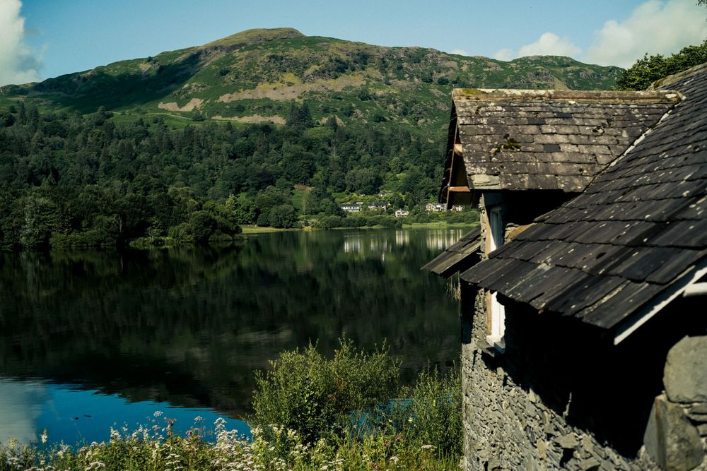 Rustic cabin roof overlooking a serene mountain lake surrounded by lush green hills.