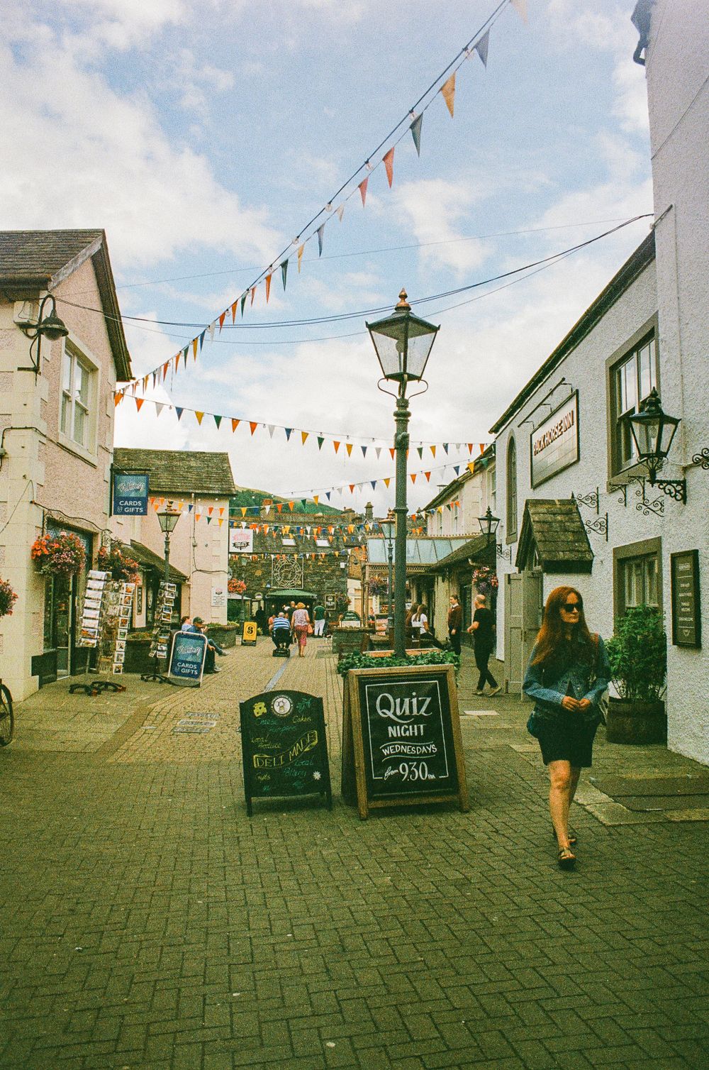 Charming village street decorated with colorful bunting flags between traditional stone buildings.