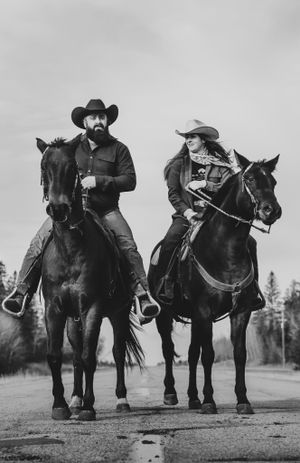 Two horse riders in cowboy attire on a country road captured in monochrome.