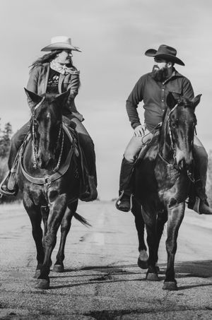 Black and white photo of two riders on horseback having a conversation while riding.