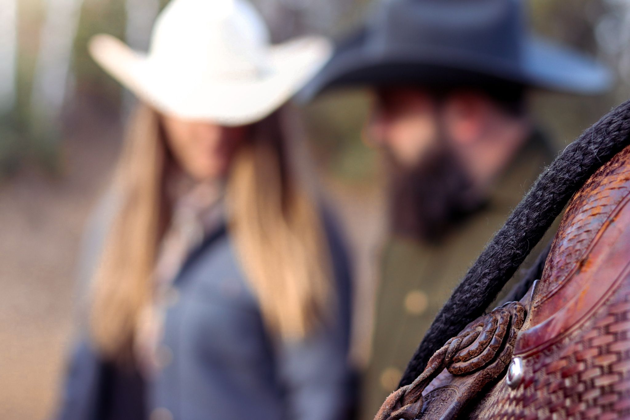 Close-up detail of a leather western saddle with riders blurred in background.
