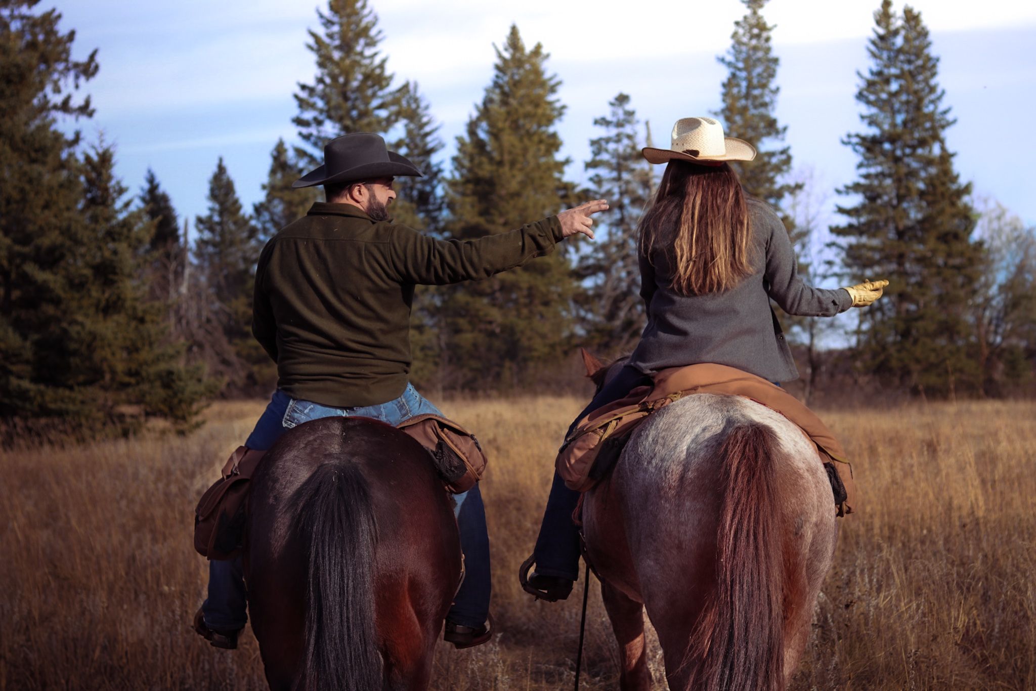 Two riders on horseback observe scenic mountain landscape with evergreen forest.