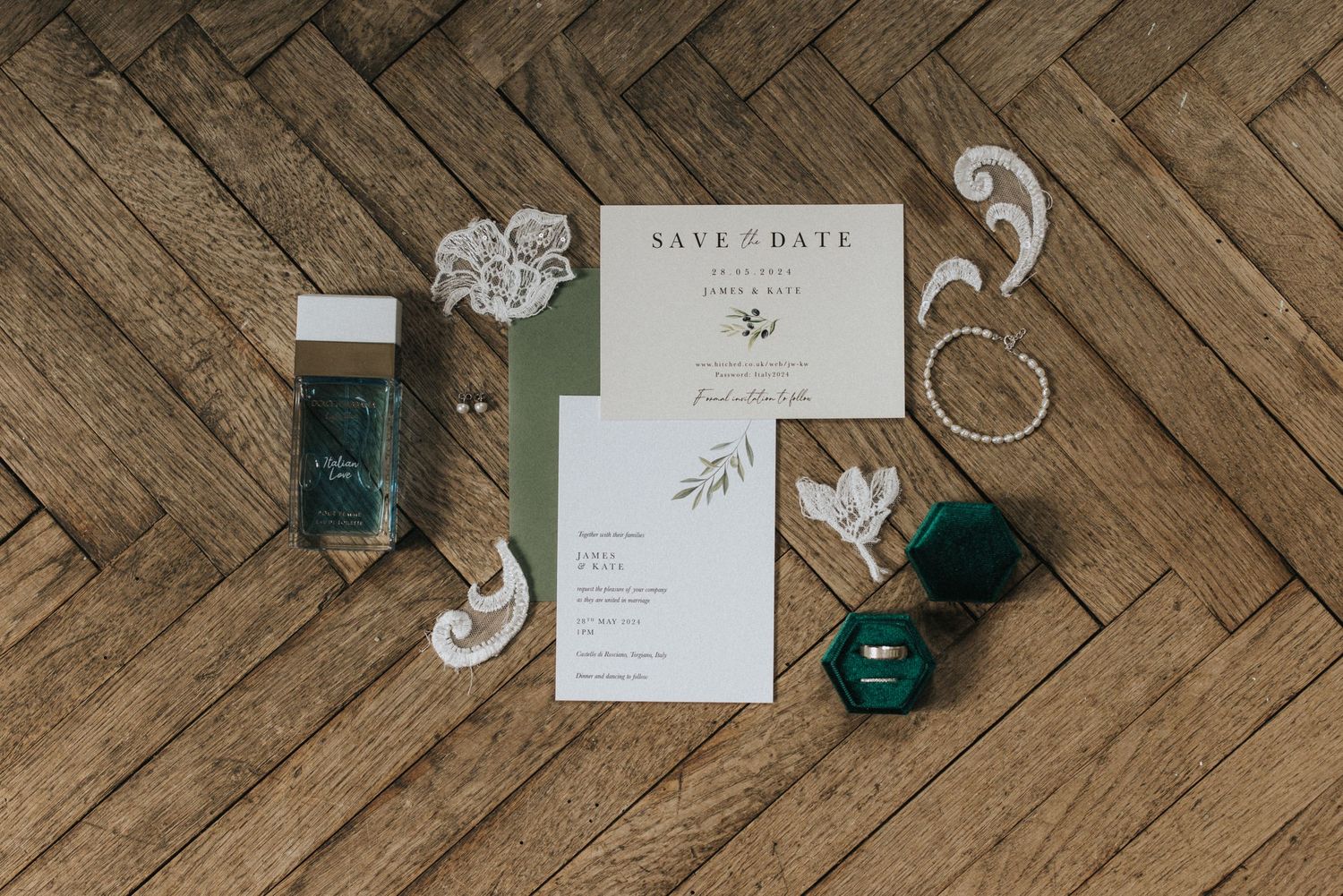 Wedding invitation suite with green accents and jewellery arranged on herringbone hardwood flooring.