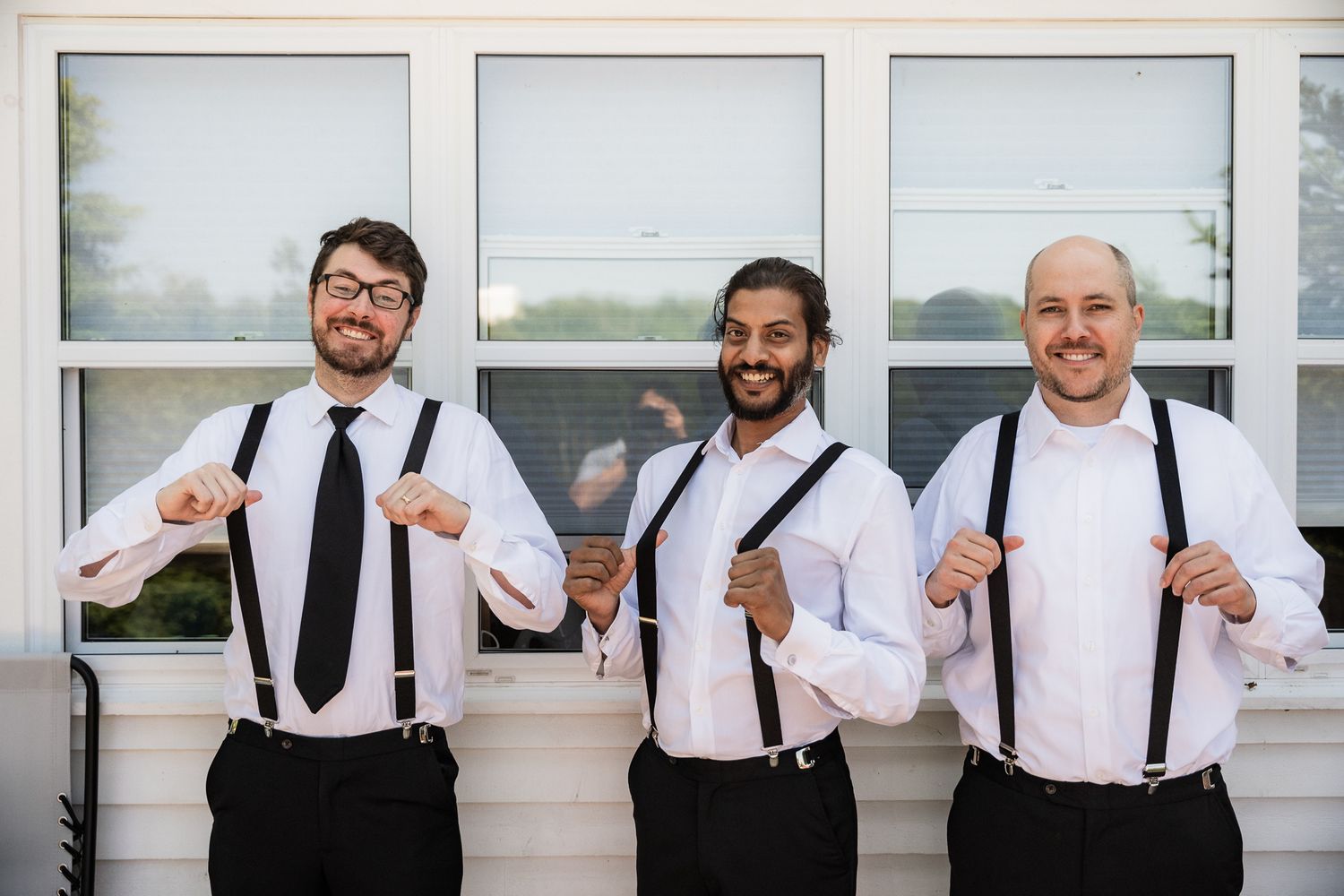 Three groomsmen laughing and playfully tugging their suspenders, full of charm and energy in St. John's, Newfoundland.