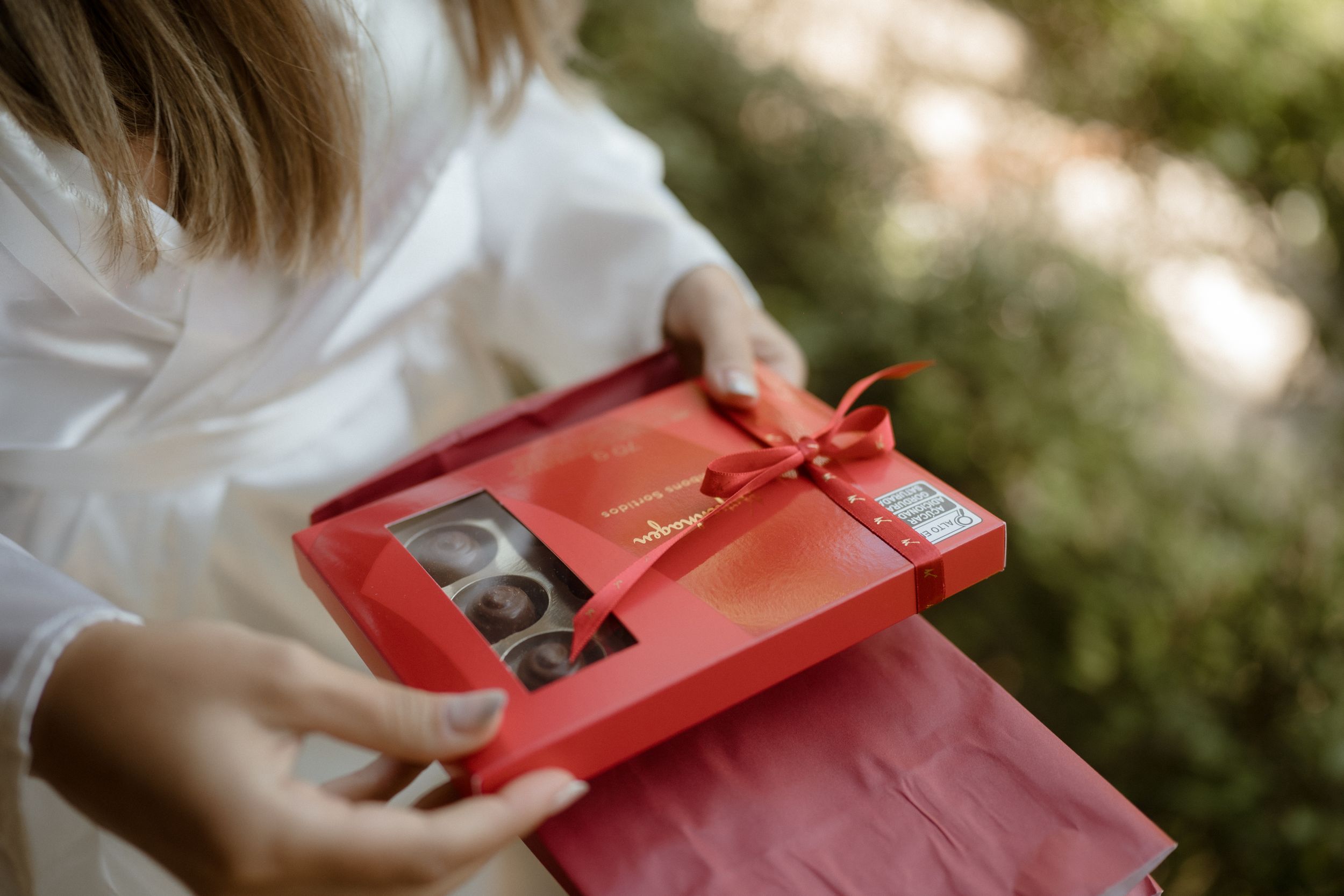 A person in white holds a red gift box while sitting outdoors.