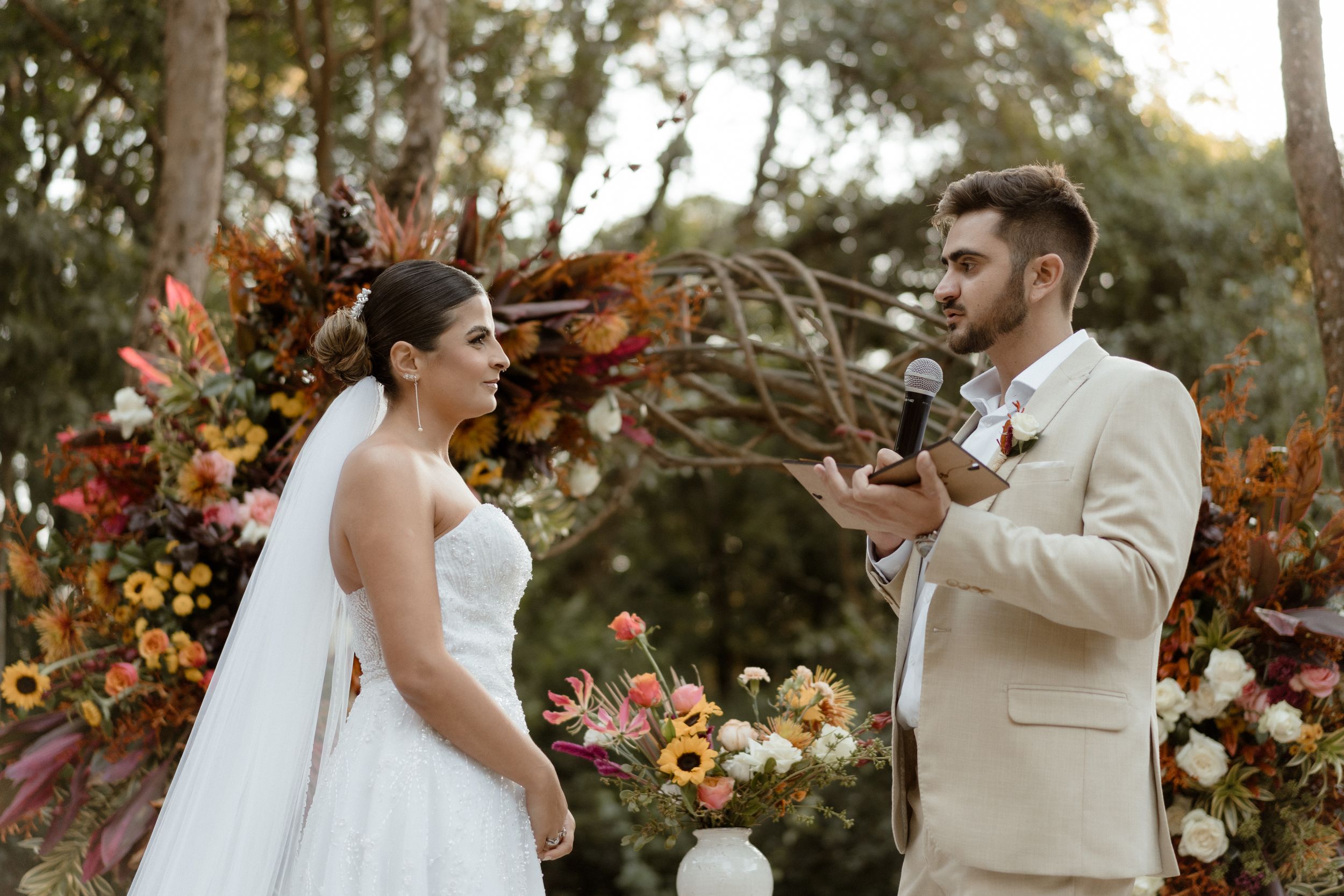 Couple exchanging vows at outdoor autumn wedding with vibrant floral arrangements.