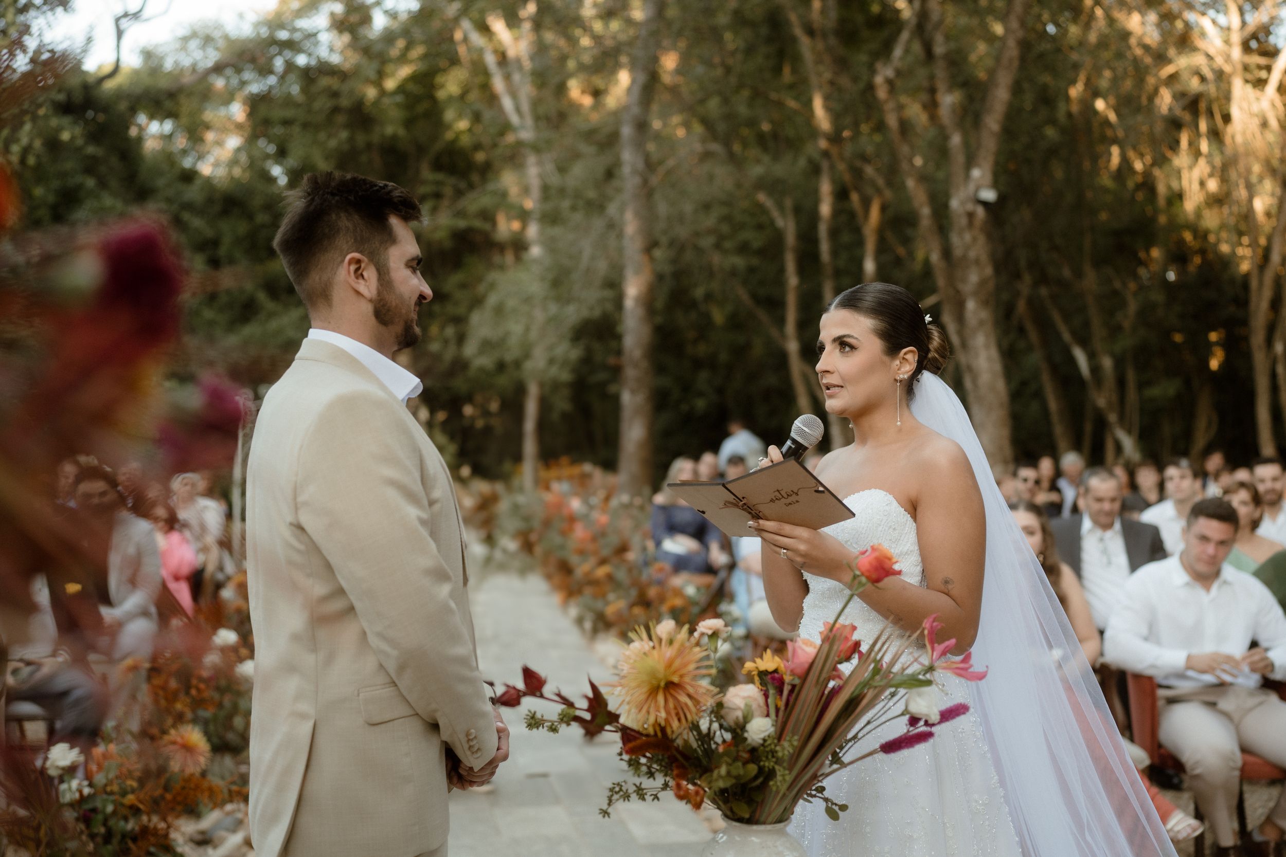 Couple exchanging vows at outdoor forest wedding with autumn-themed floral decorations.