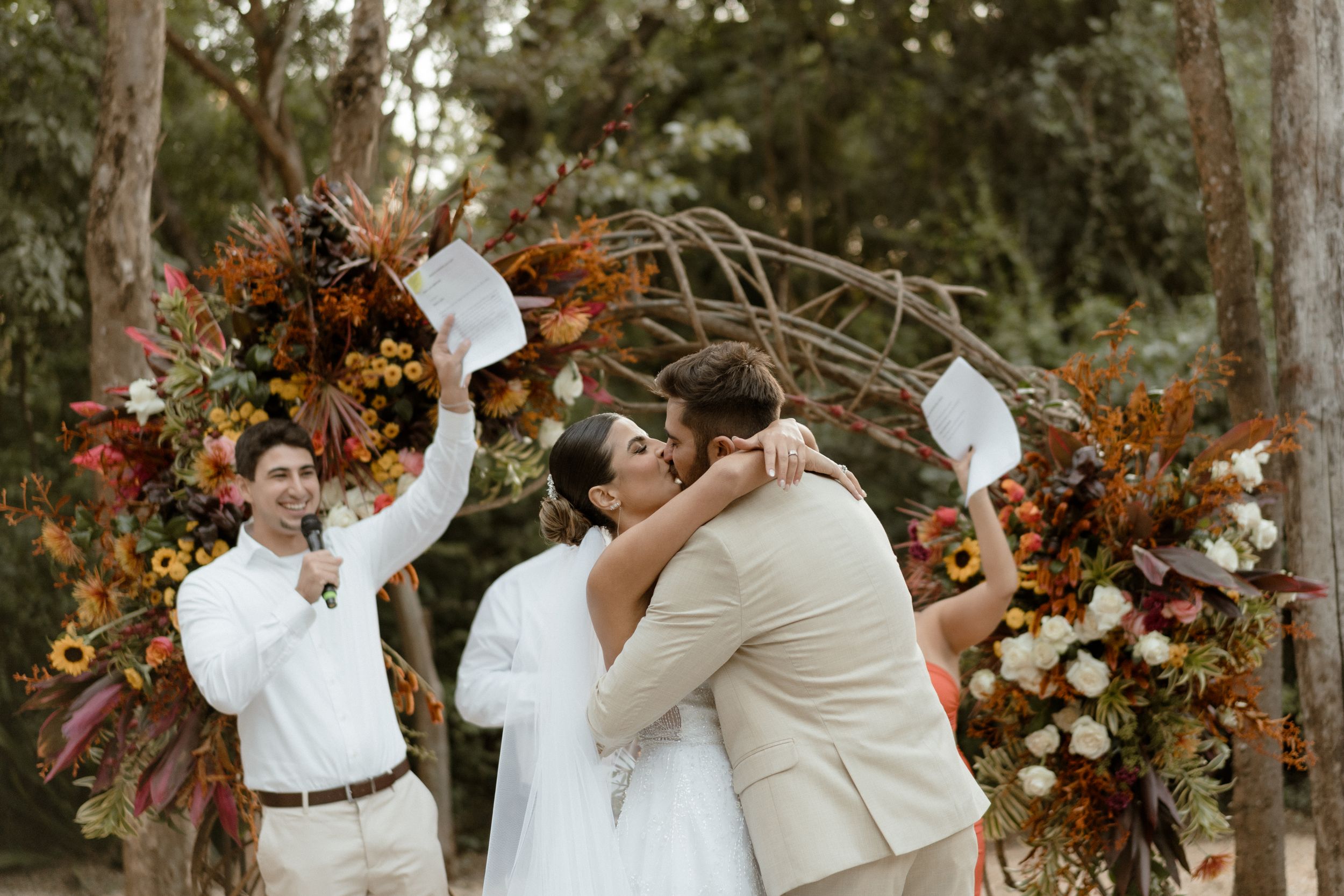 Wedding party celebrates outdoors with autumnal floral arrangements and decorative iron gates.