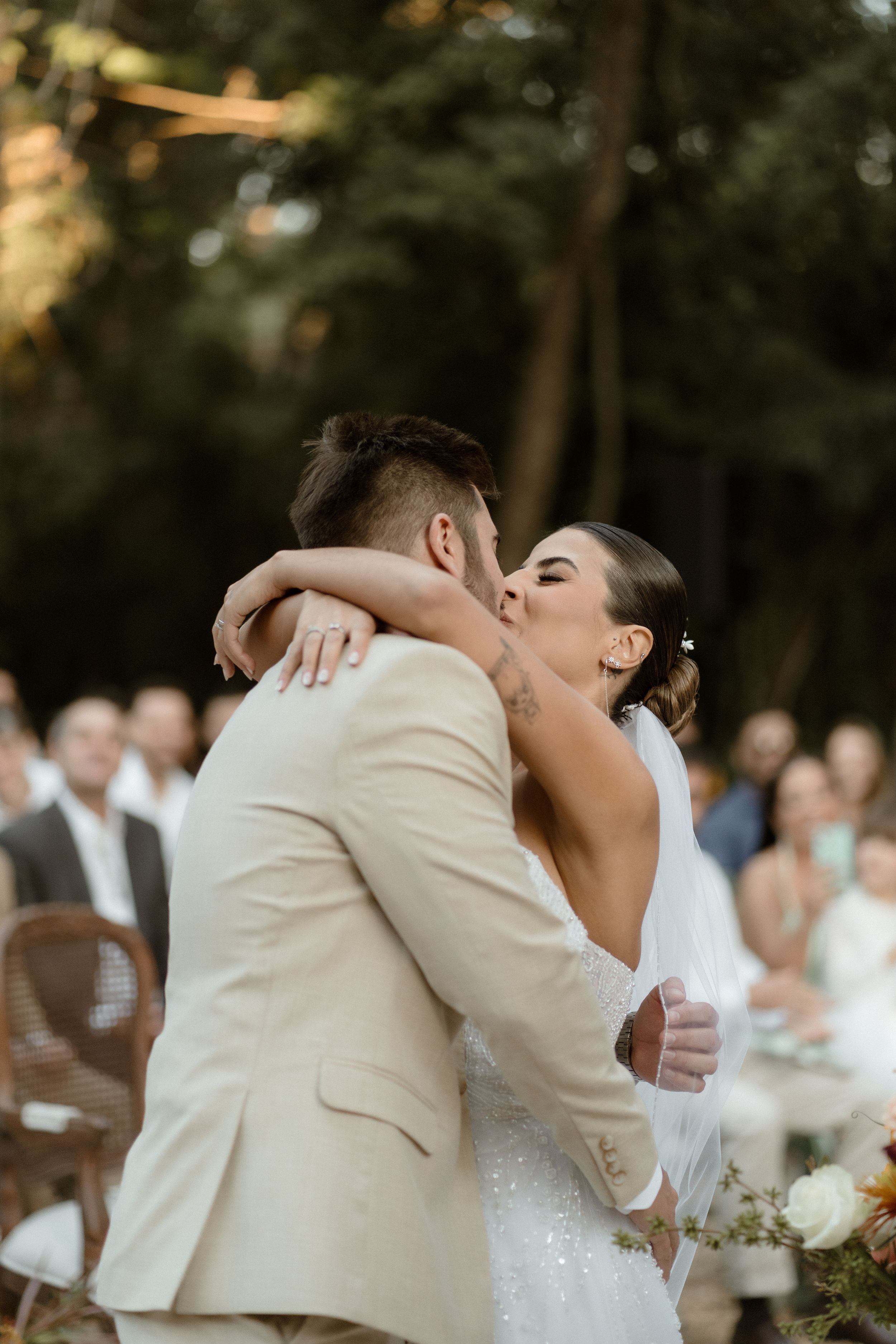 Romantic wedding moment captured during outdoor ceremony with guests in background.