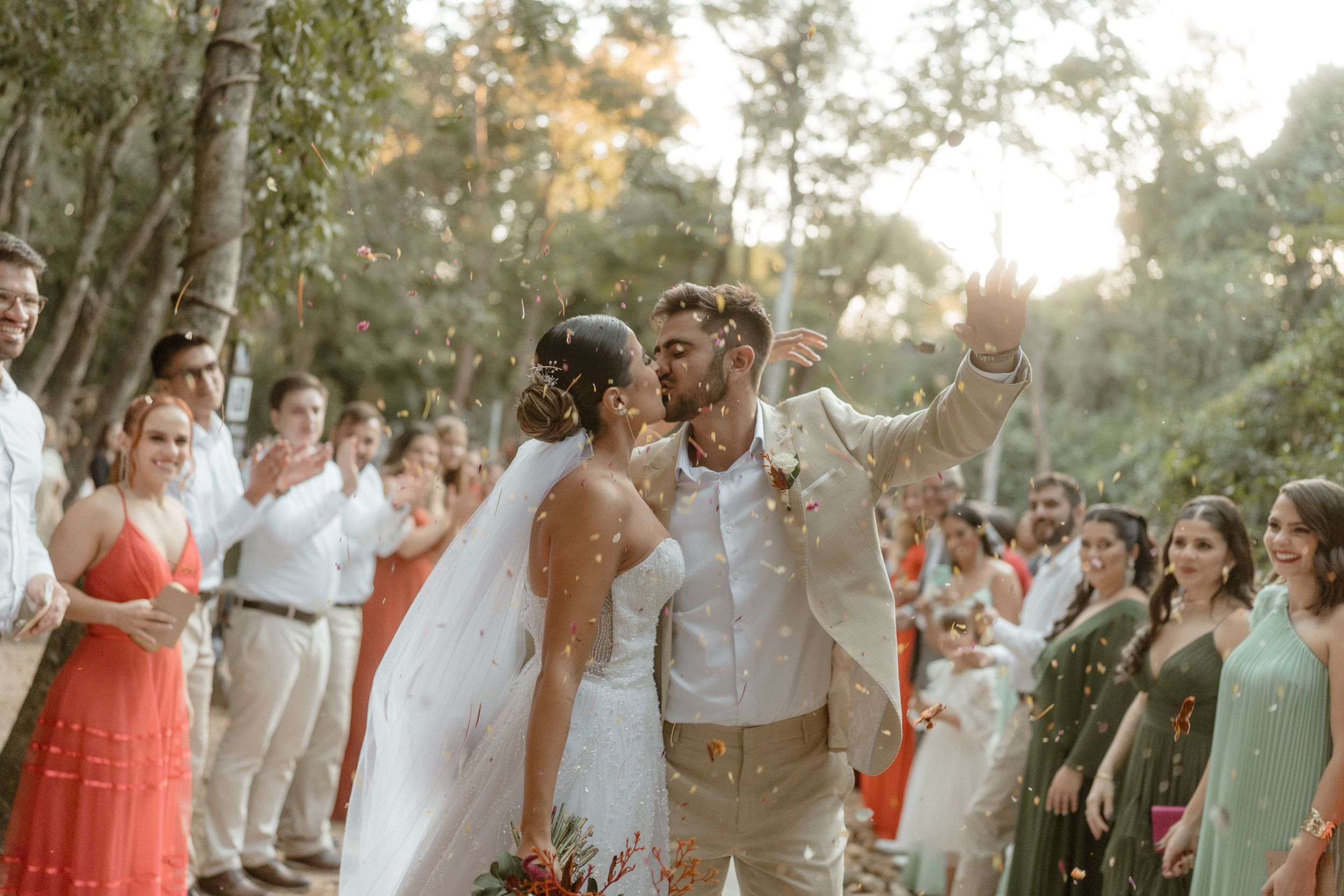 Wedding party and guests line up outdoors against natural forest backdrop.