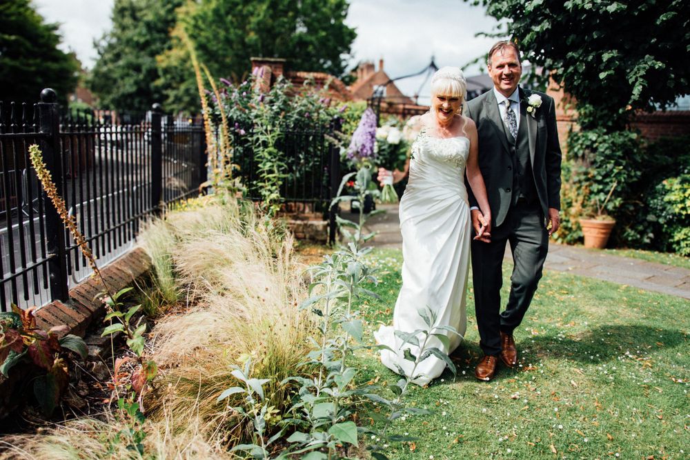 Couple strolling through a landscaped garden with decorative grasses and iron fencing.
