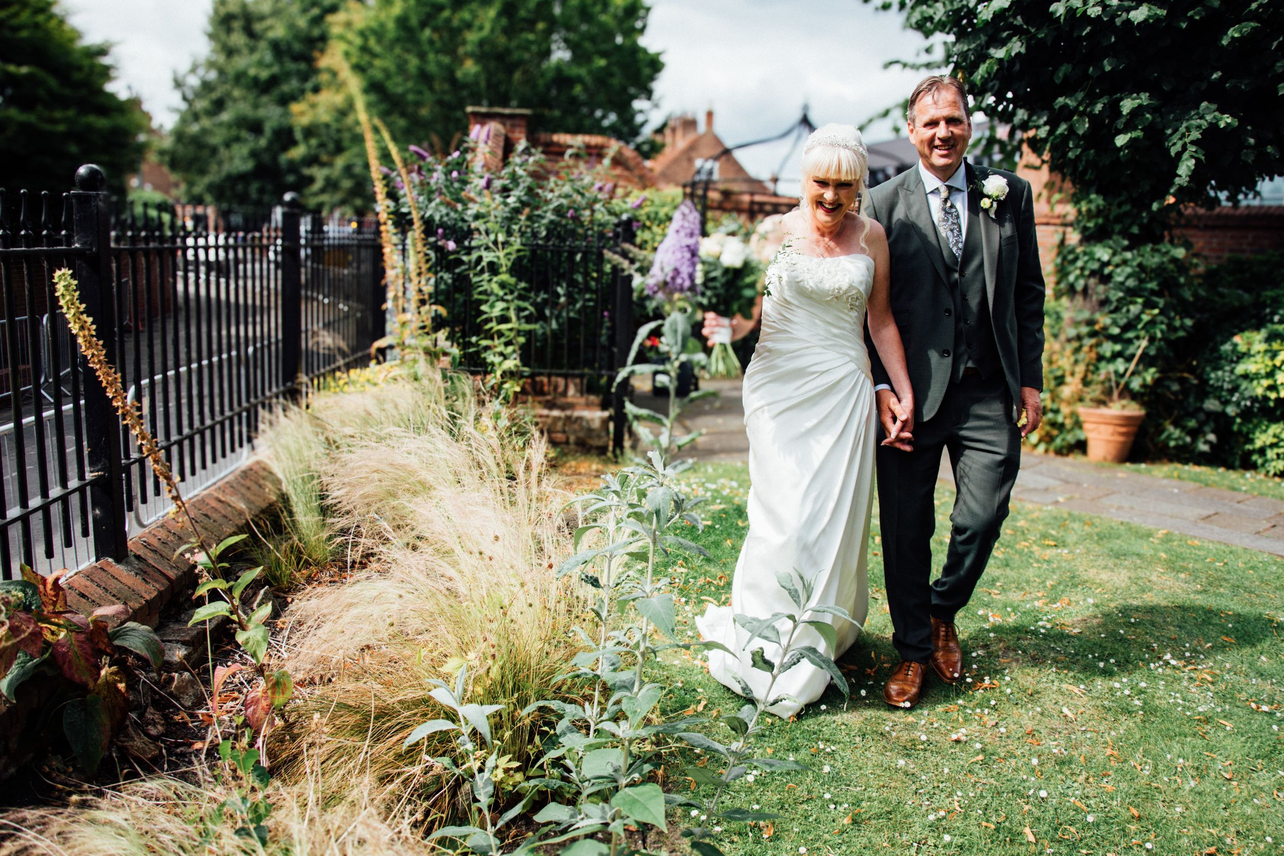 Couple strolling through a landscaped garden with decorative grasses and iron fencing.