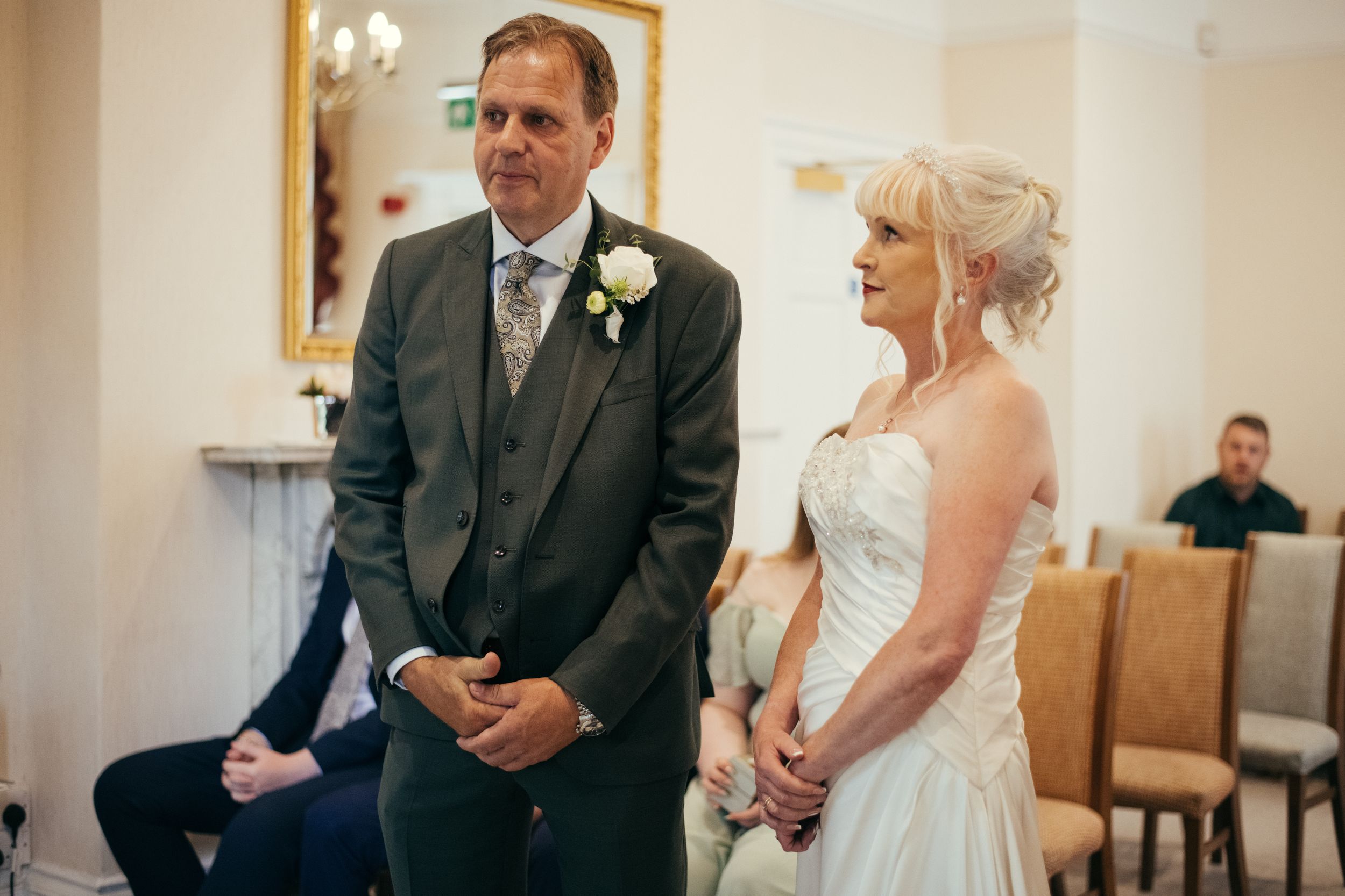 Wedding ceremony in progress in an elegant white room with fireplace.