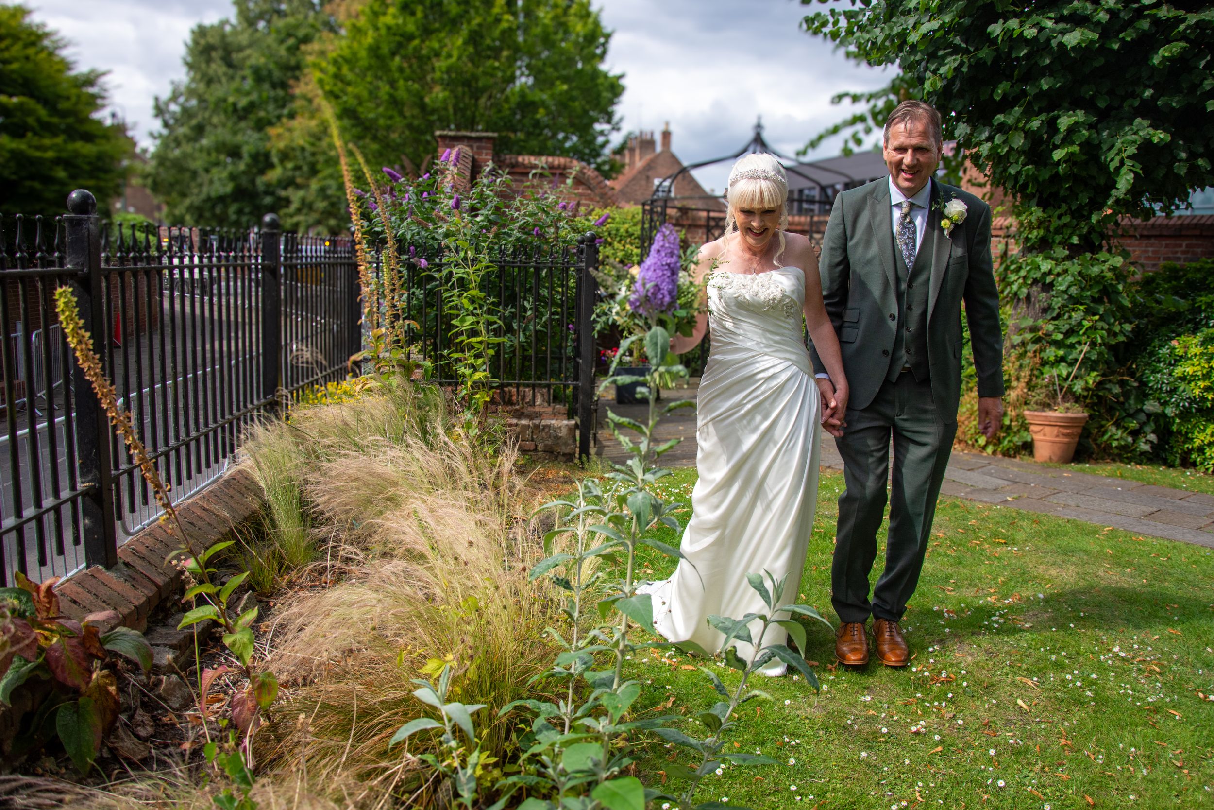 A newlywed couple walking along a garden path with ornamental grasses.
