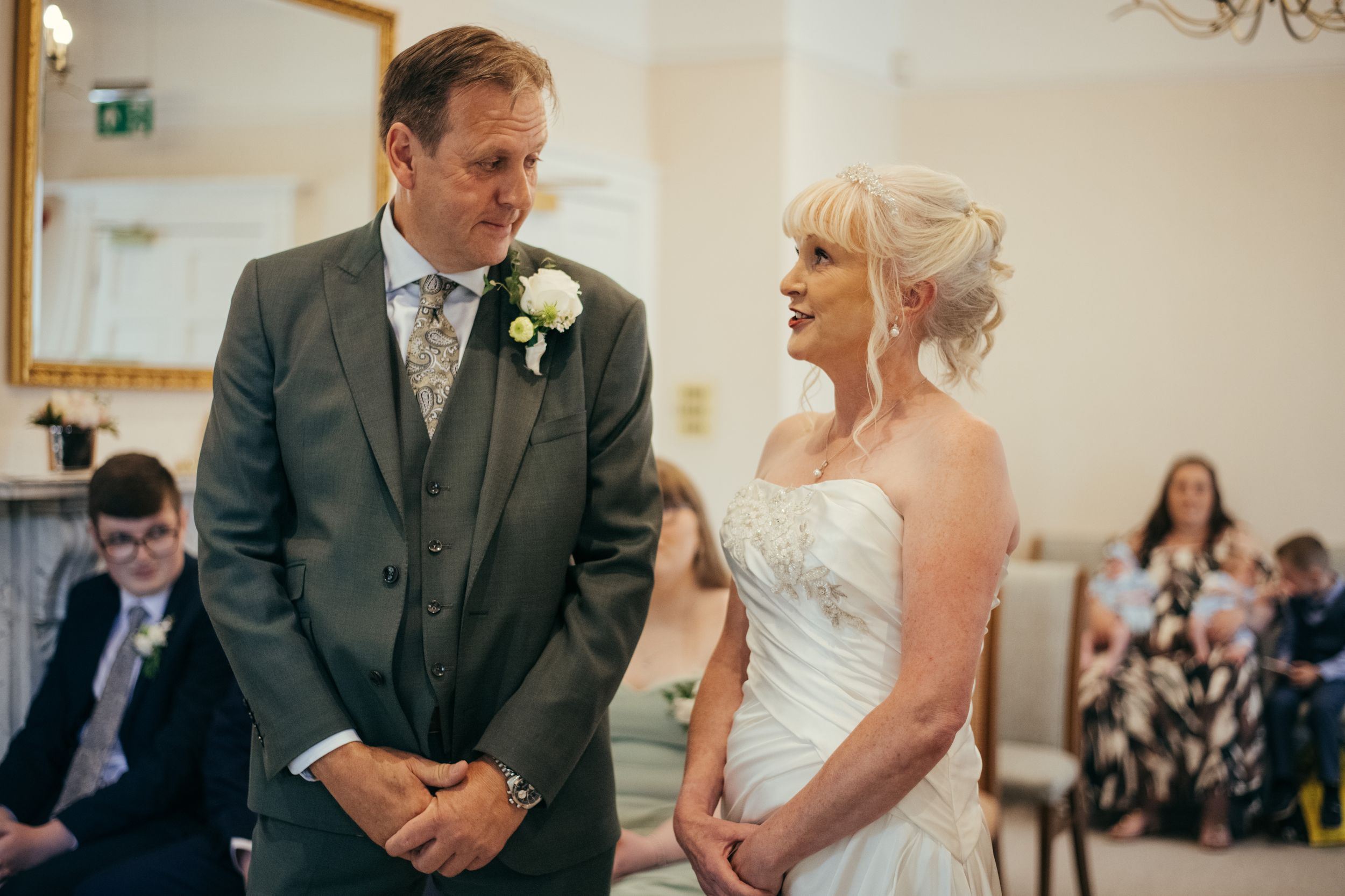 Wedding ceremony taking place in an elegant white room with decorative mirrors.