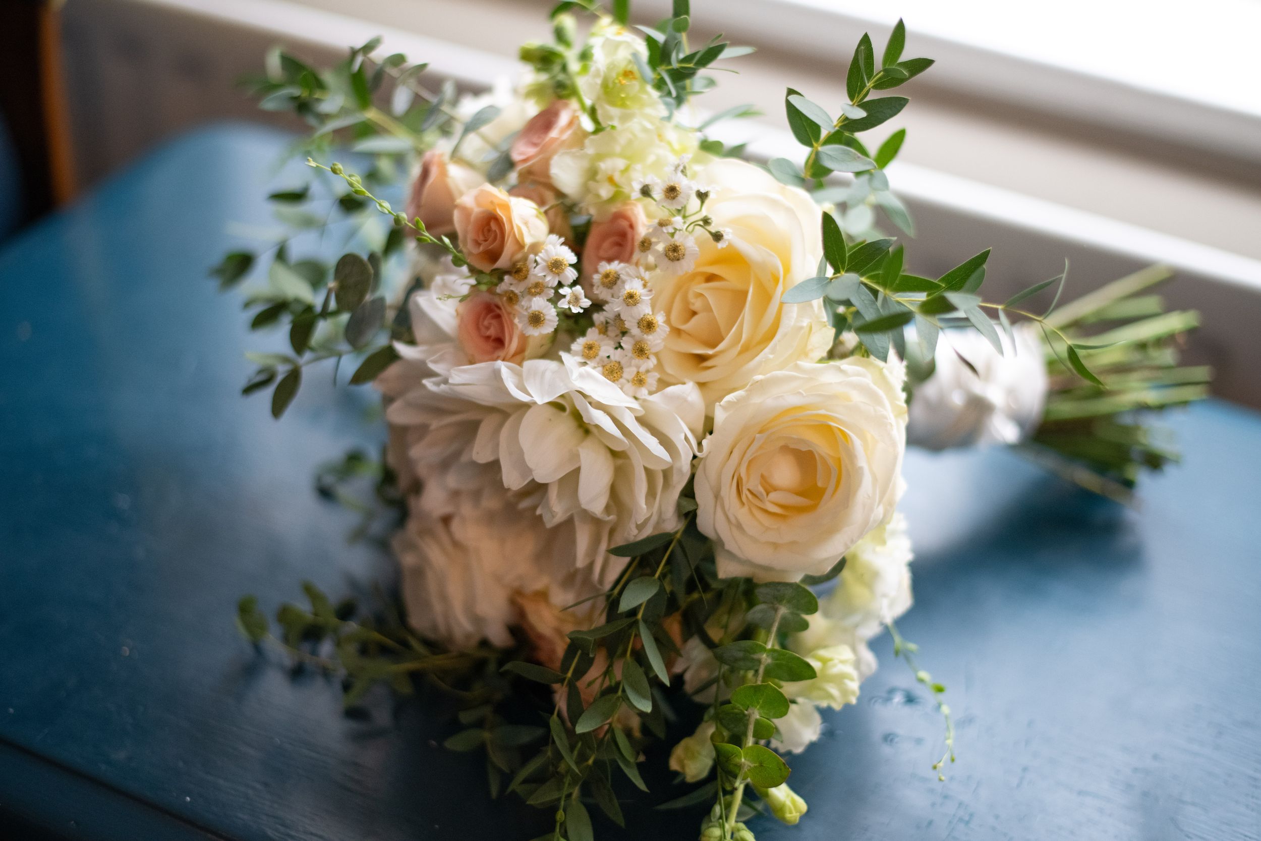 Wedding bouquet with cream roses and green foliage on a blue surface.