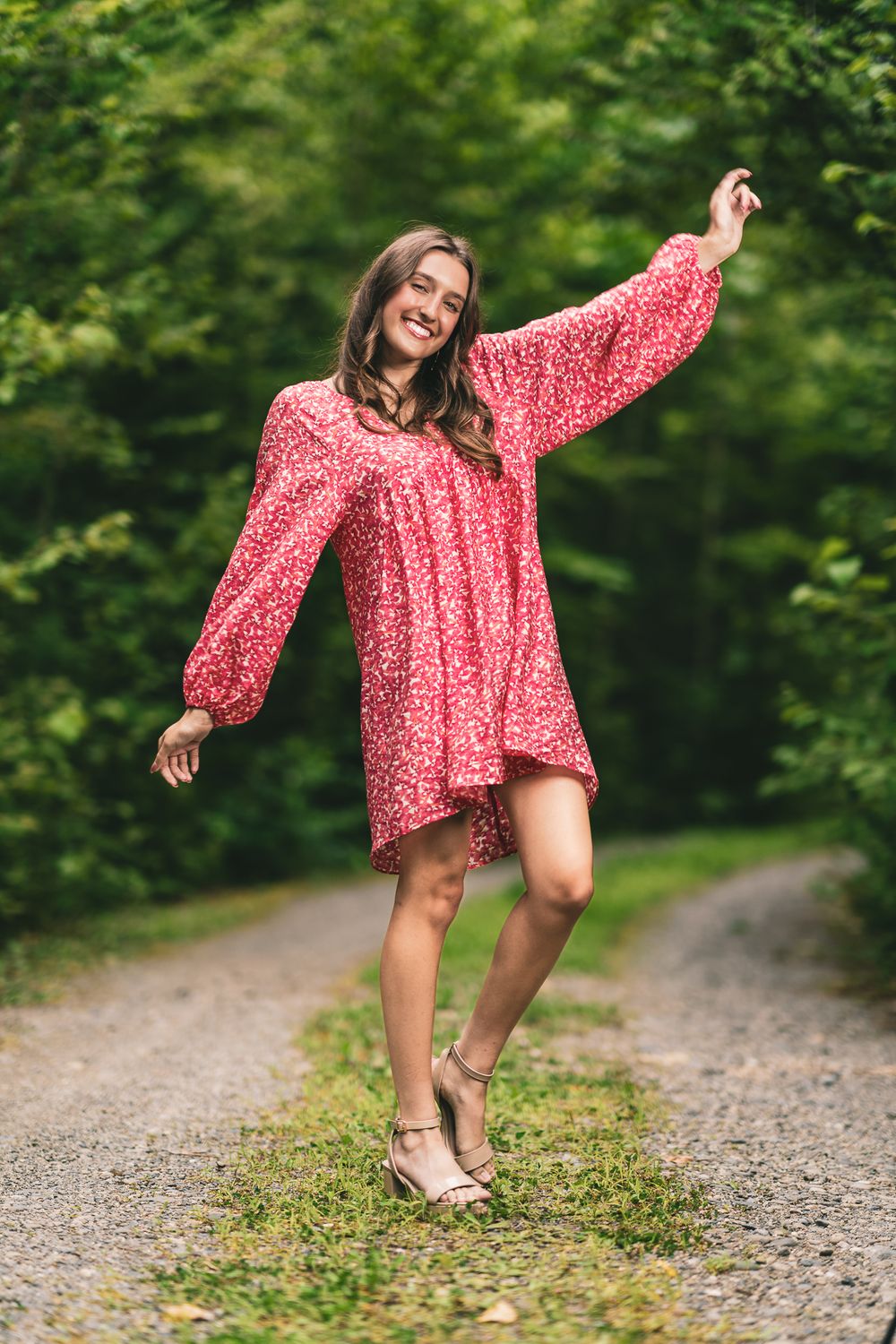 Woman in flowing red floral dress dancing joyfully on a forest path.