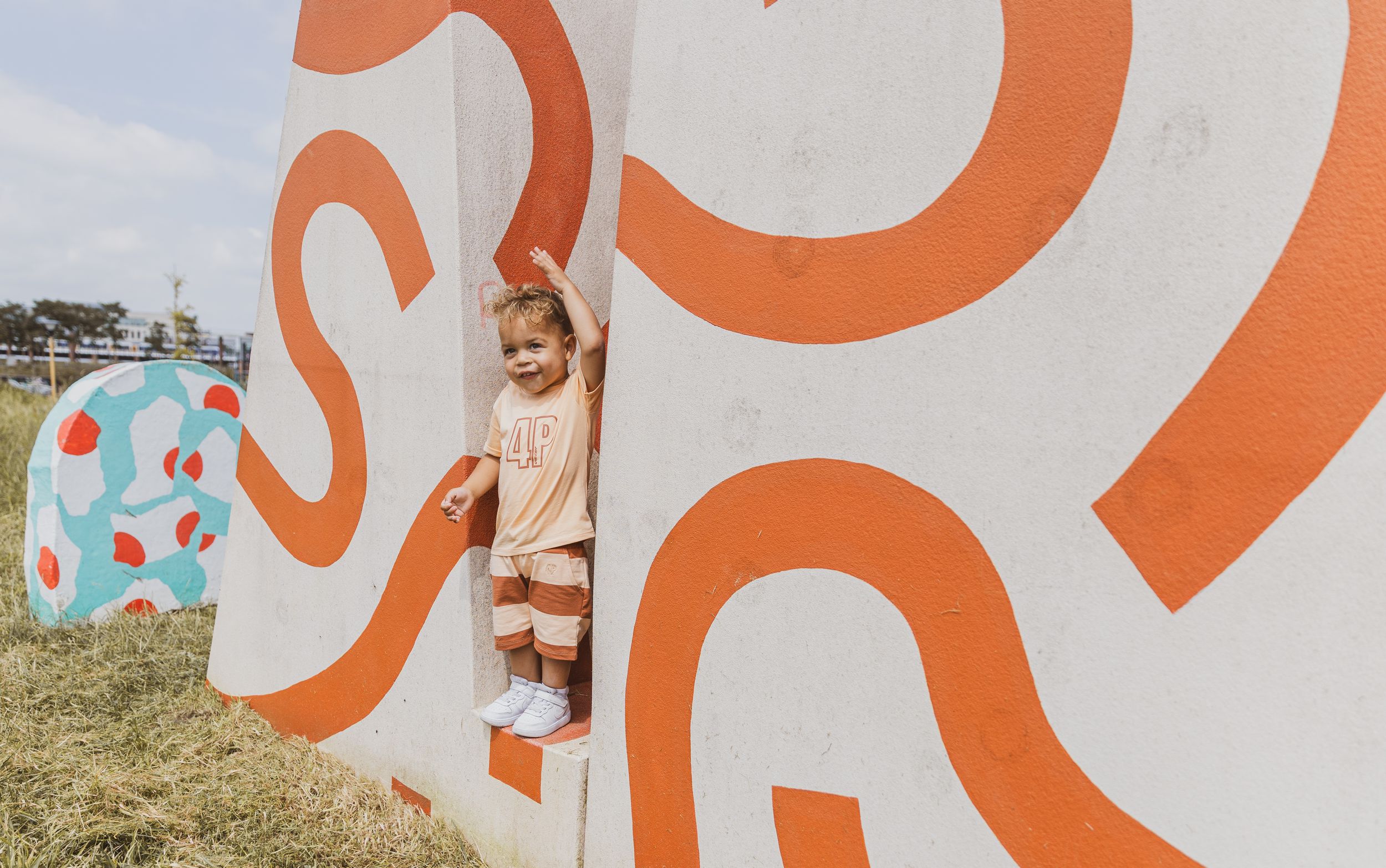 Toddler playing between colorful orange and white painted walls with swirl designs outdoors.