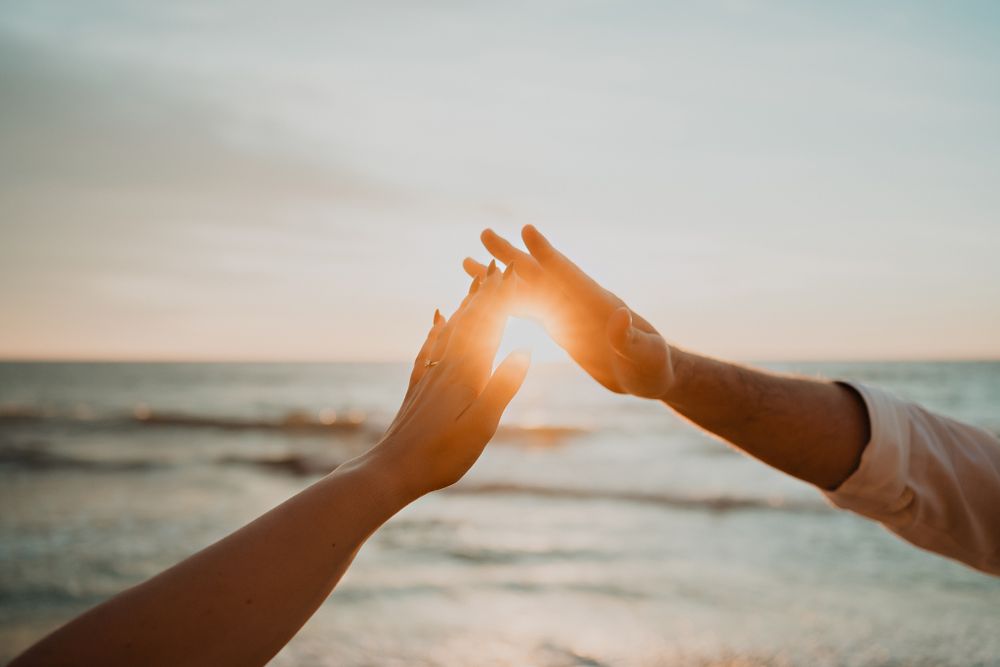 Their hands reaching towards the sun, a symbolic connection during their beach shoot