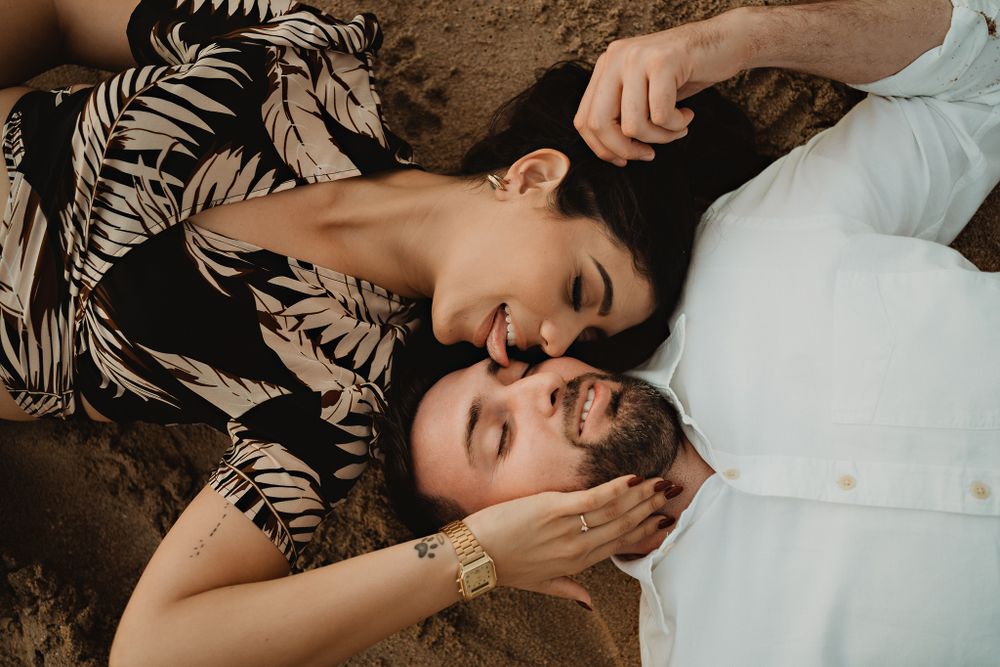 The couple lying on the sand, playful and spontaneous, capturing their joyful connection
