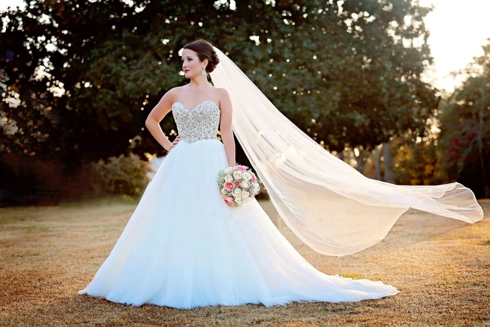 Elegant wedding dress with flowing tulle skirt and long veil captured in golden sunset light outdoors.