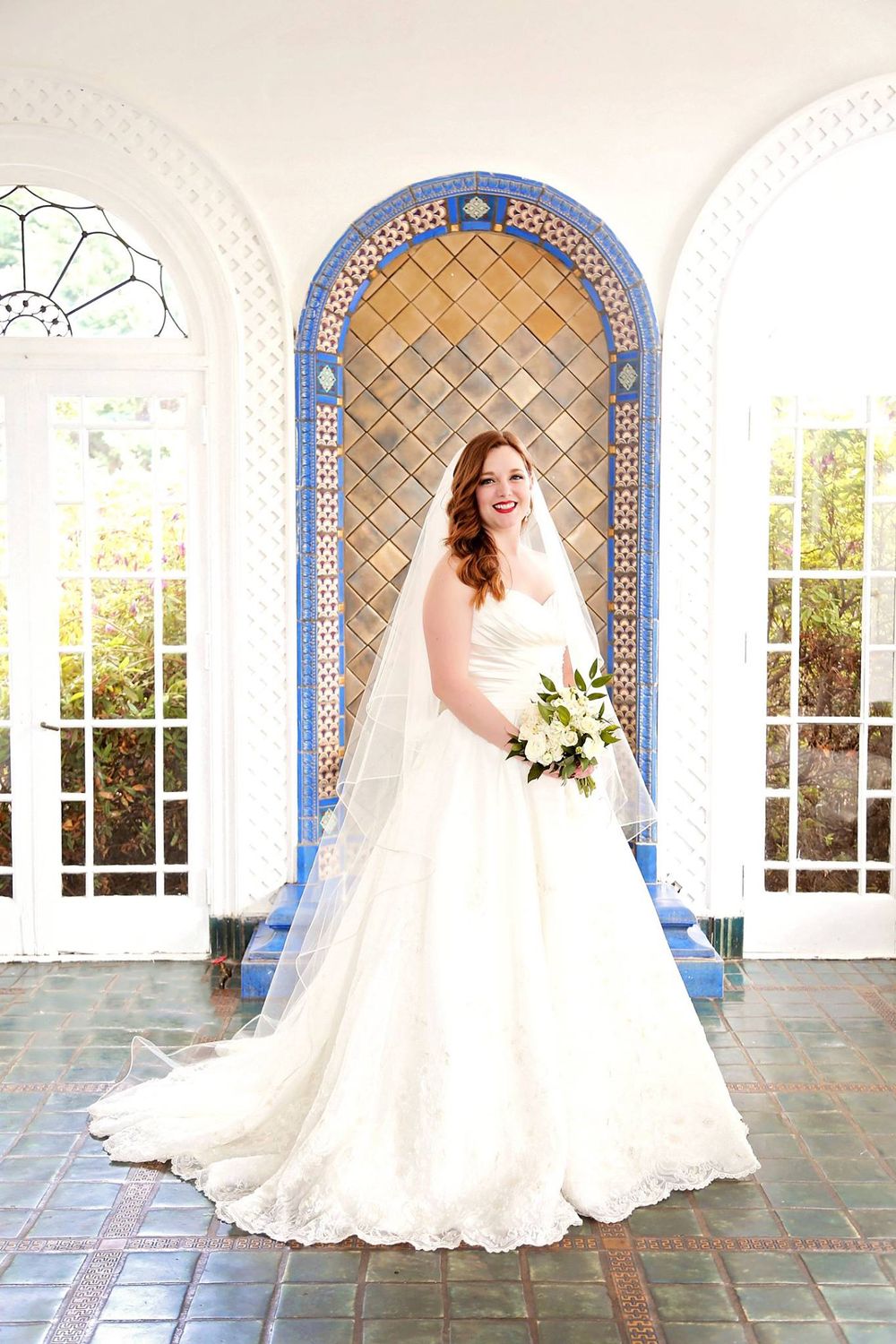 Beautiful bridal portrait in white gown under ornate blue archway.