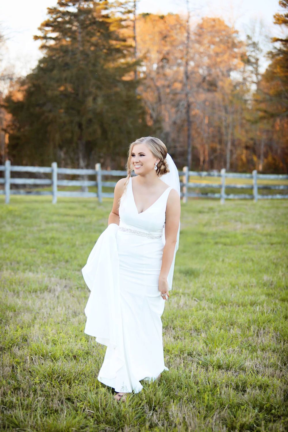 Simple elegant wedding dress photographed in rustic field with wooden fence backdrop.