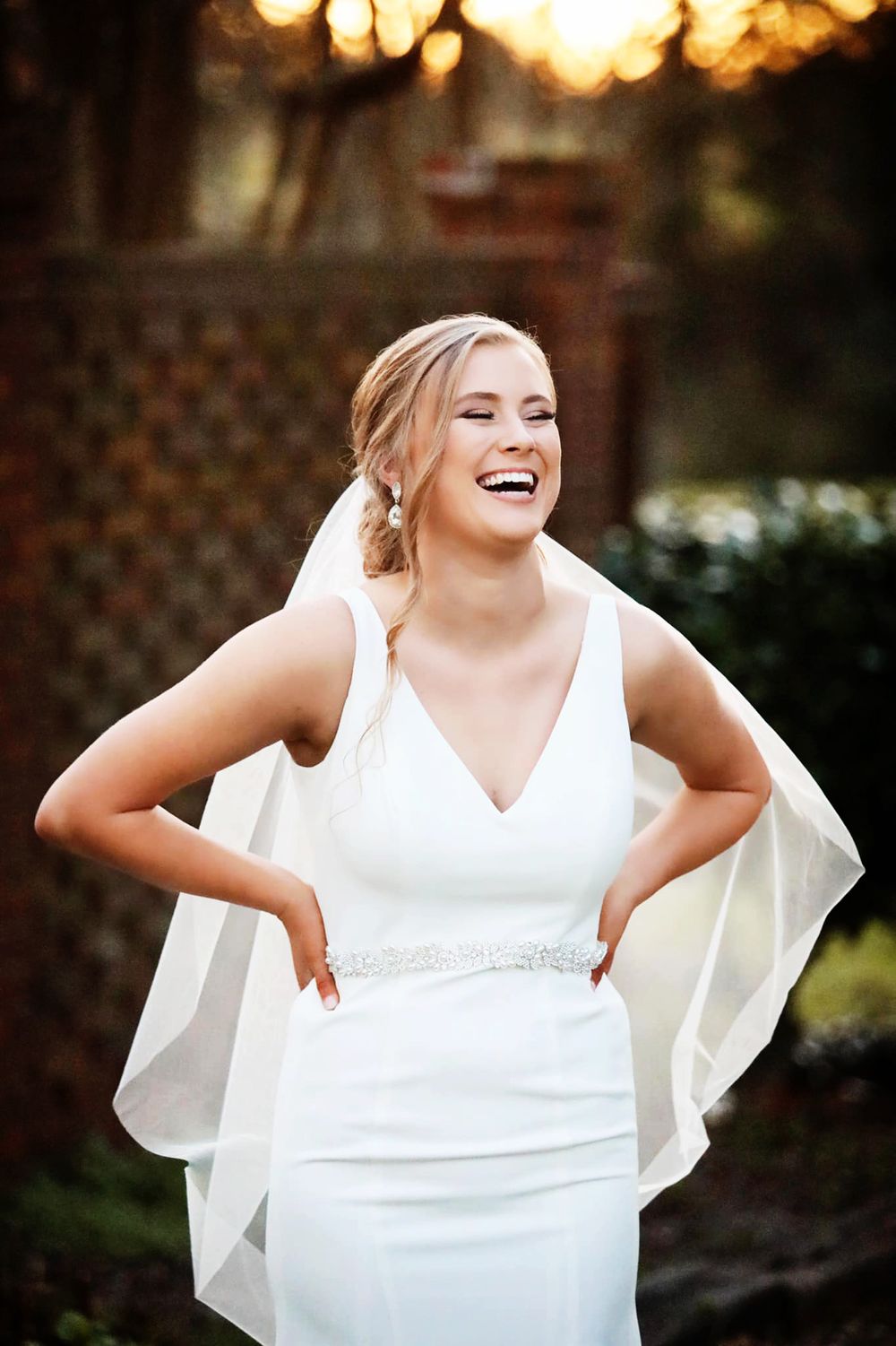 Joyful wedding portrait in fitted white gown with sheer veil at sunset.