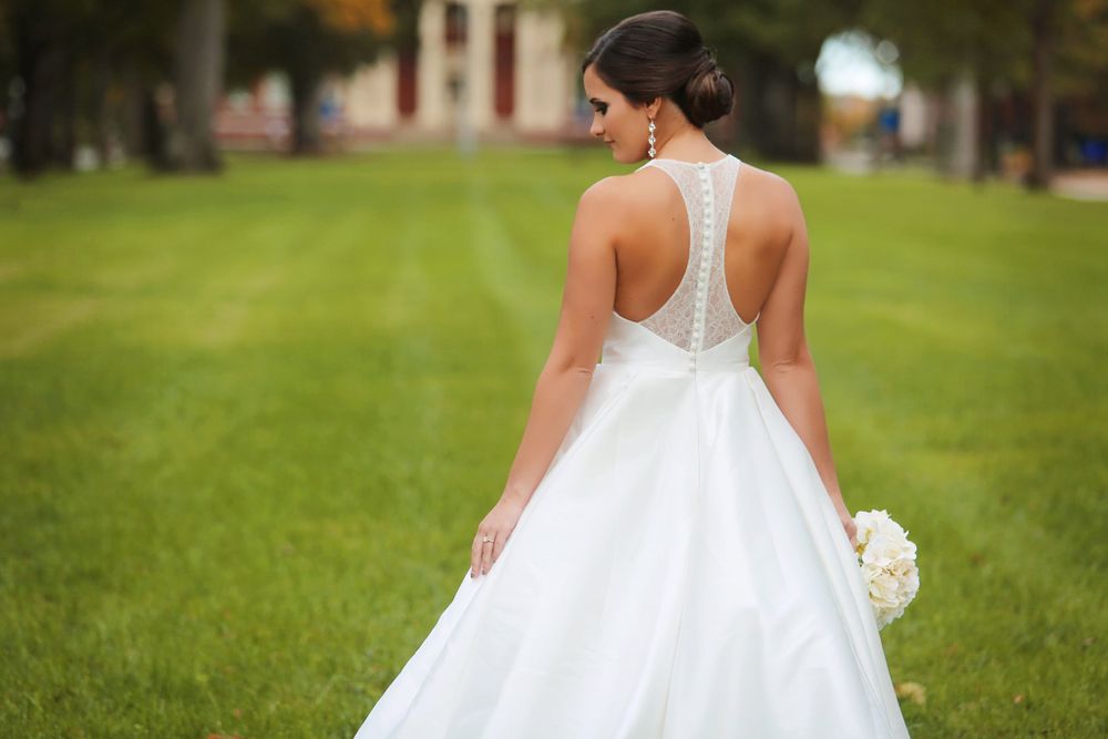 Elegant white wedding dress with detailed lace back shown on grassy lawn.