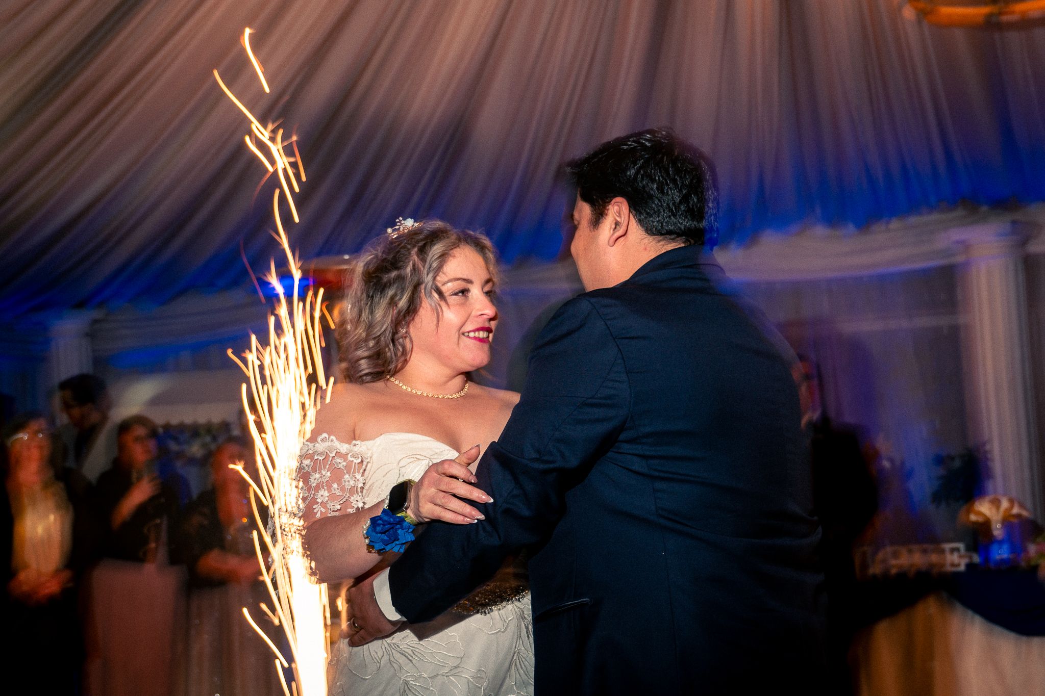 Fiesta de matrimonio con baile bajo iluminación azul y bengalas creando atmósfera mágica.