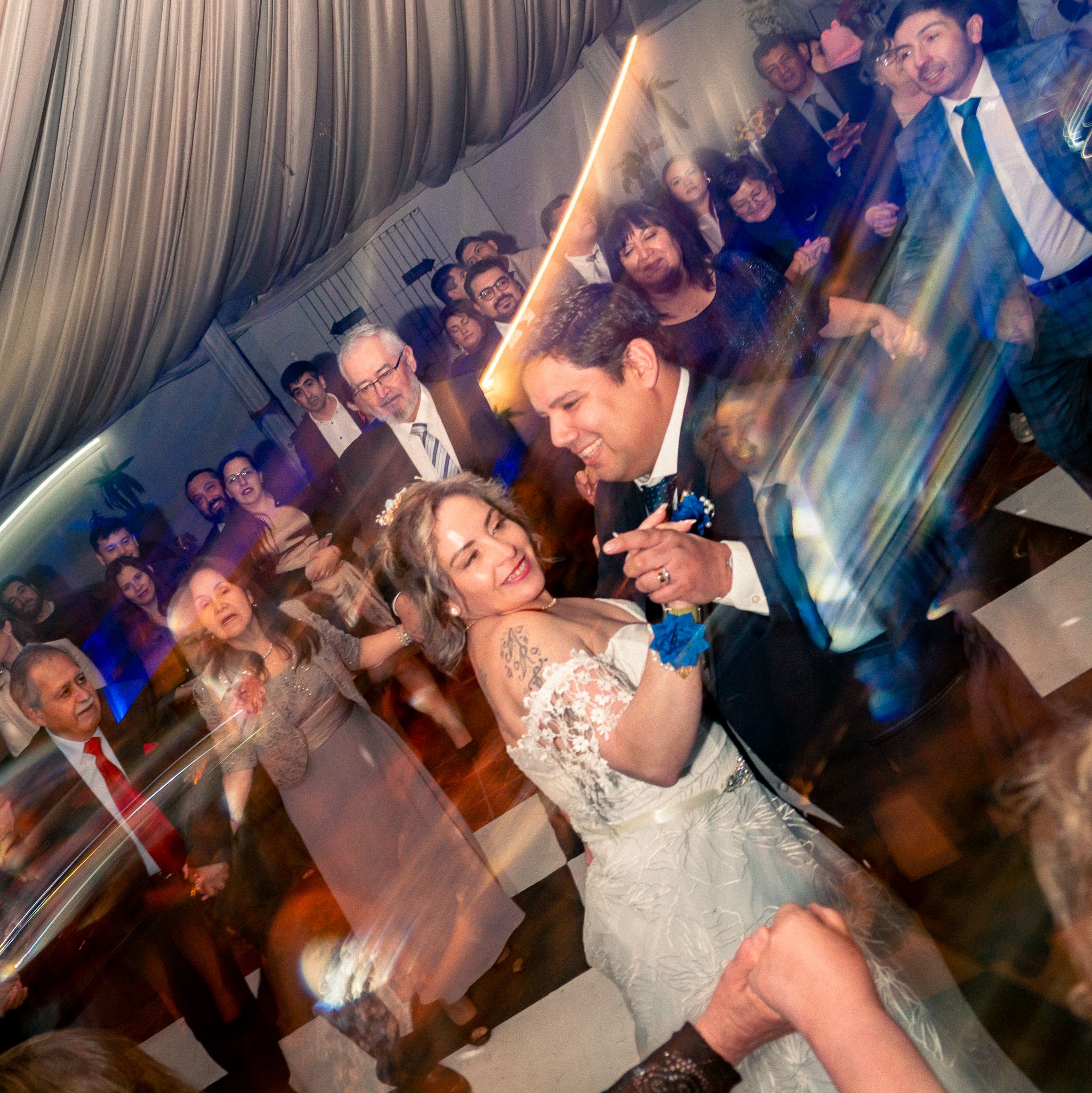 Invitados celebrando en pista de baile llena durante recepción de matrimonio nocturna con iluminación dramática.