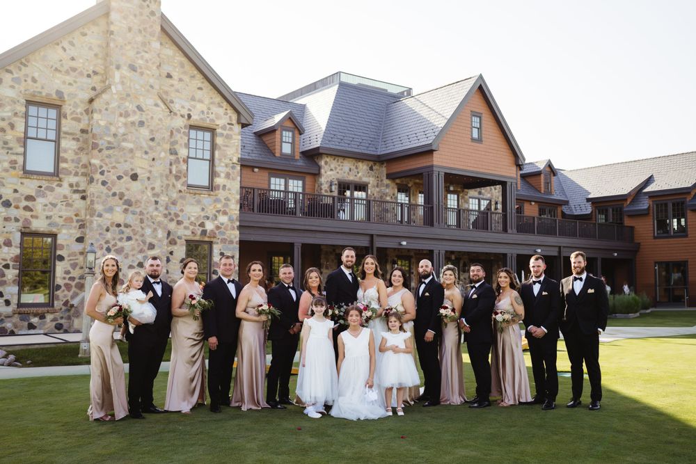 Wedding party poses for formal group photo in front of rustic stone and brick venue.