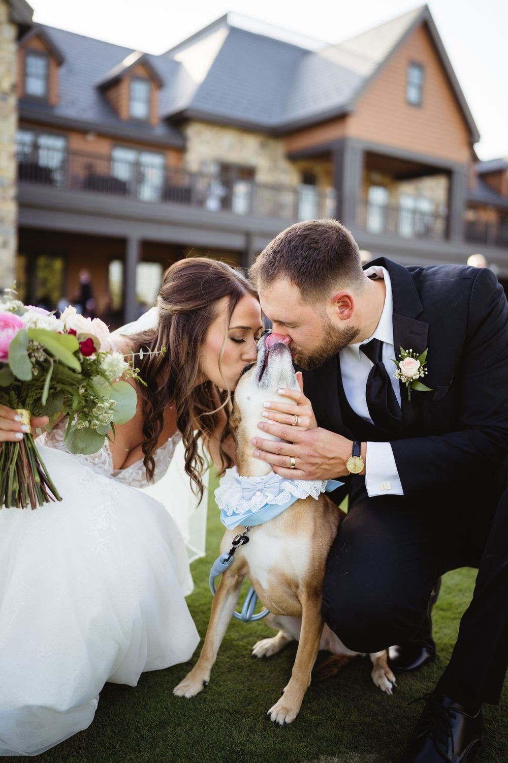 Couple shares intimate moment with their dog during wedding photoshoot on lawn.