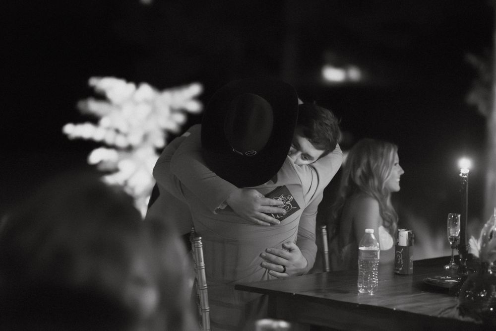 Black and white candid moment of wedding couple embracing during evening reception.