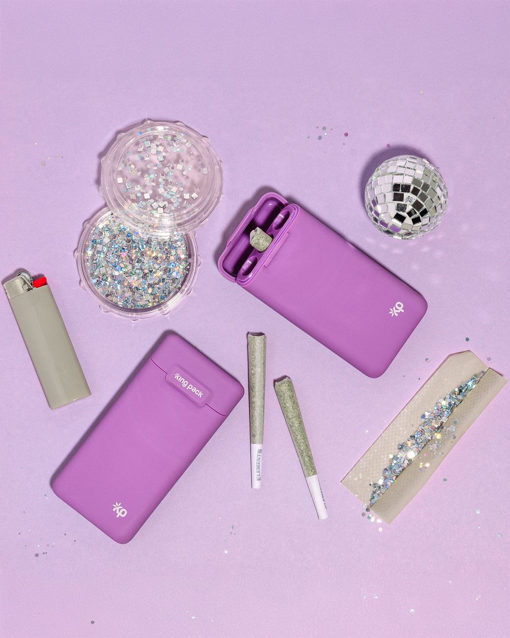 Purple vape devices with glittery disco balls and accessories on pink background.