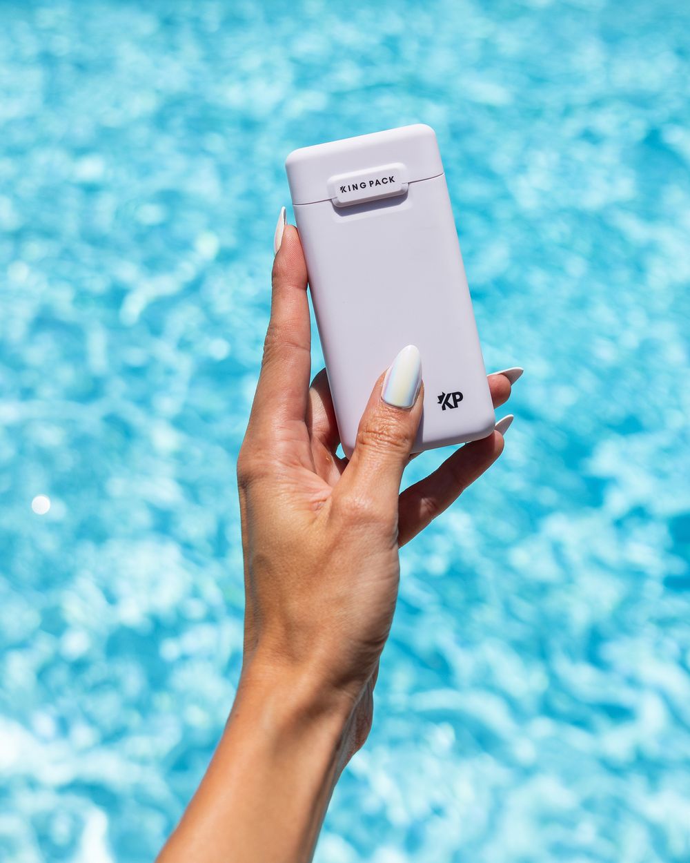 Hand holding silver portable device against blue pool water background.