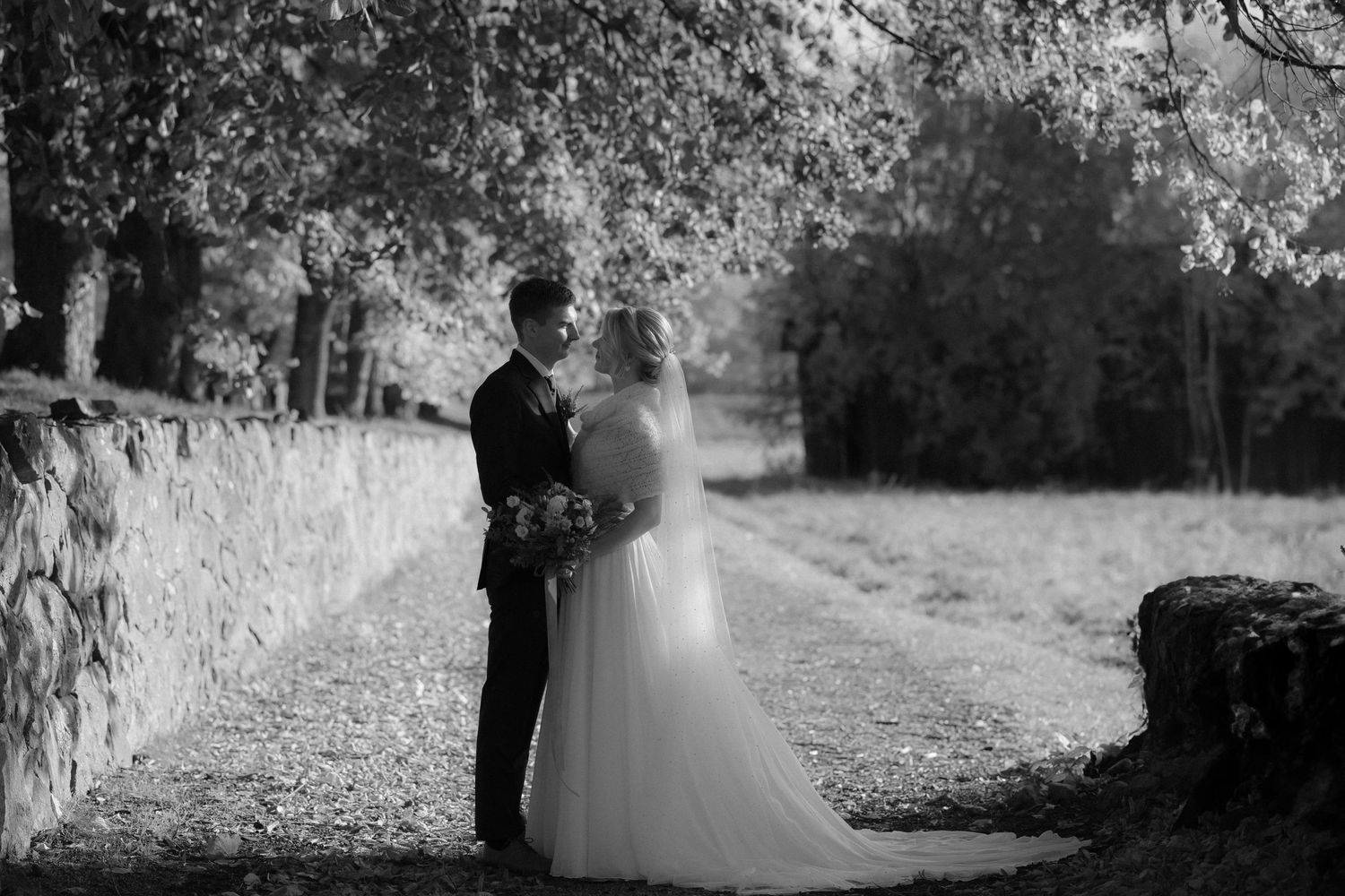 A romantic black and white wedding photo of a couple on a stone path surrounded by trees.