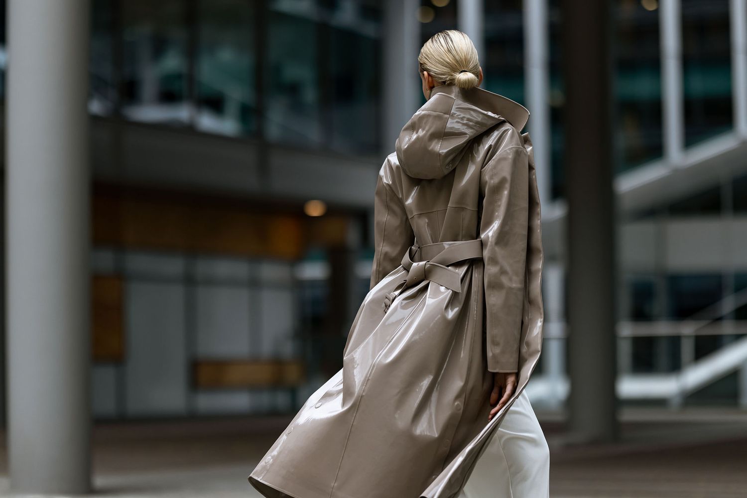 Back view of elegant beige trench coat with belted waist against modern architecture.