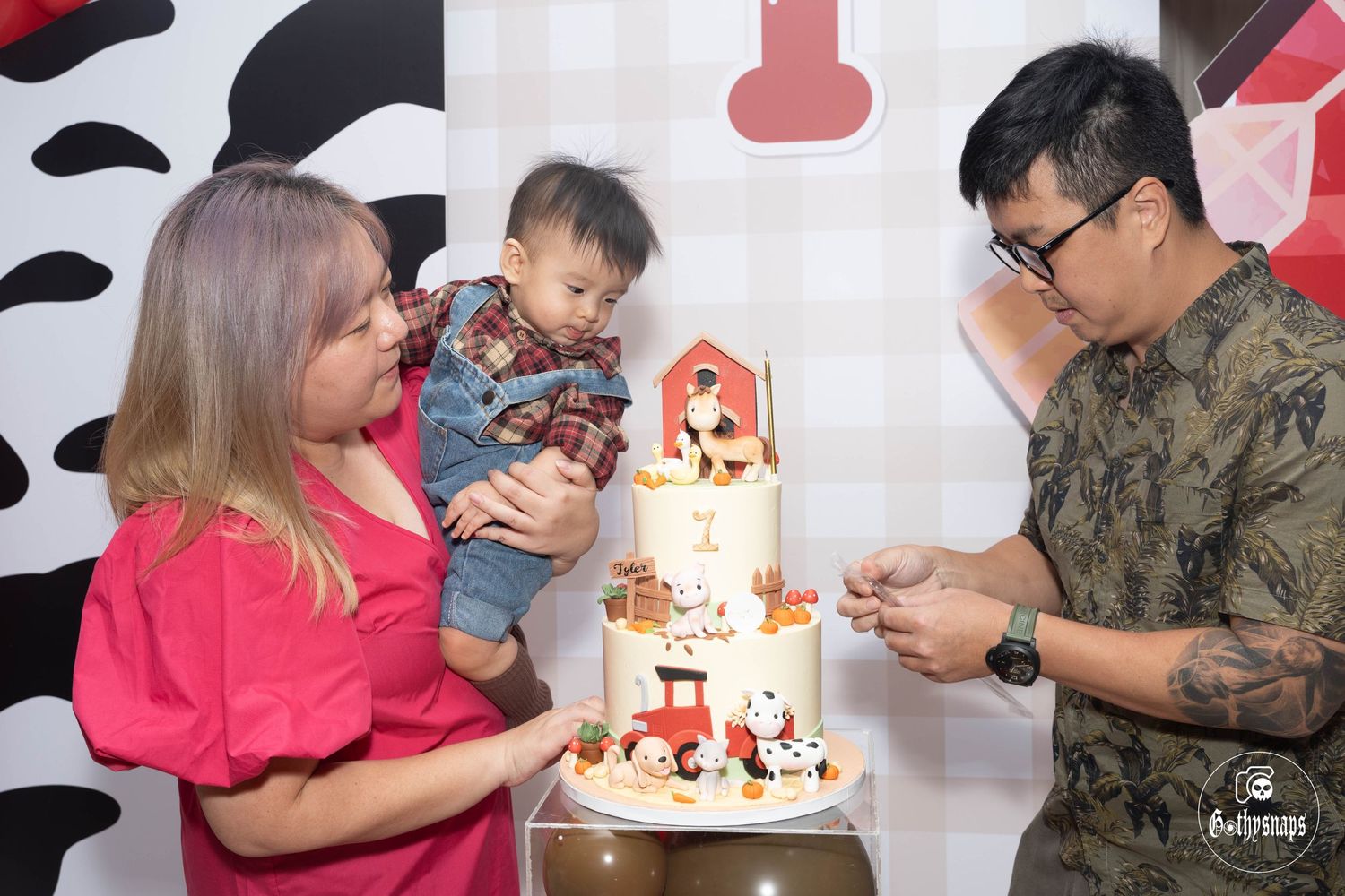 People gather around a festive birthday cake with red decorations against a black and white patterned backdrop.
